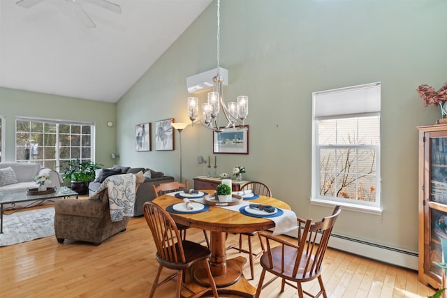 dining area with a baseboard heating unit, ceiling fan with notable chandelier, high vaulted ceiling, and light wood finished floors