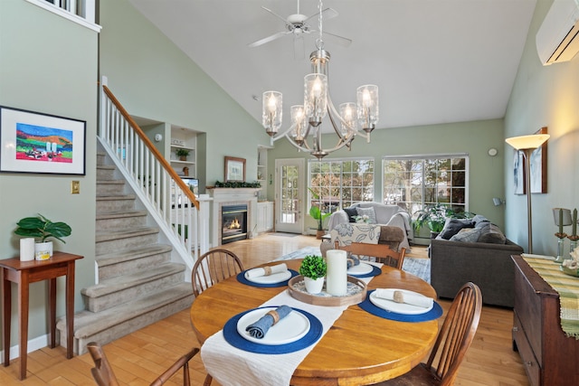 dining space with a wall unit AC, stairway, high vaulted ceiling, light wood-style flooring, and a glass covered fireplace