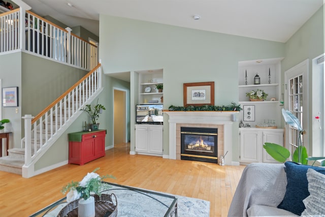 living room with built in shelves, baseboards, a fireplace, stairs, and light wood-type flooring