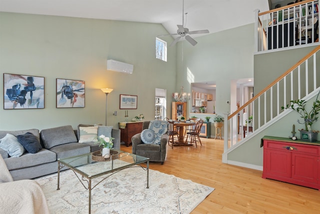 living area with ceiling fan with notable chandelier, stairway, light wood-style floors, baseboards, and a towering ceiling