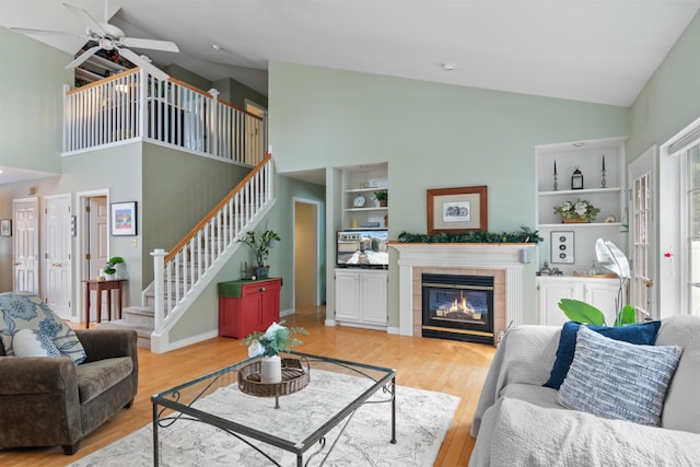 living area with built in shelves, a tiled fireplace, light wood-type flooring, stairs, and vaulted ceiling