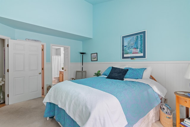 carpeted bedroom featuring a high ceiling, a wainscoted wall, and connected bathroom