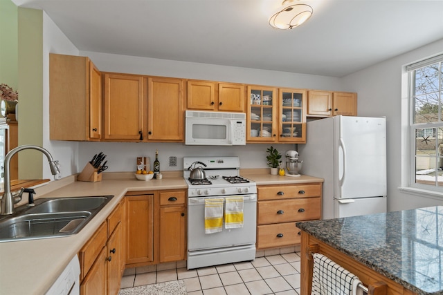 kitchen featuring a sink, white appliances, brown cabinetry, light tile patterned floors, and glass insert cabinets