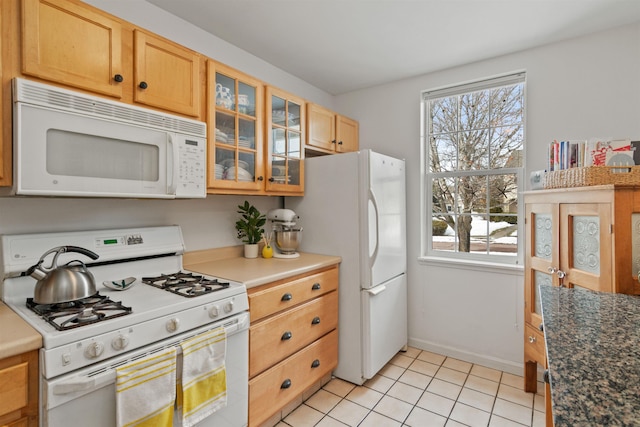 kitchen featuring dark countertops, glass insert cabinets, baseboards, light tile patterned floors, and white appliances