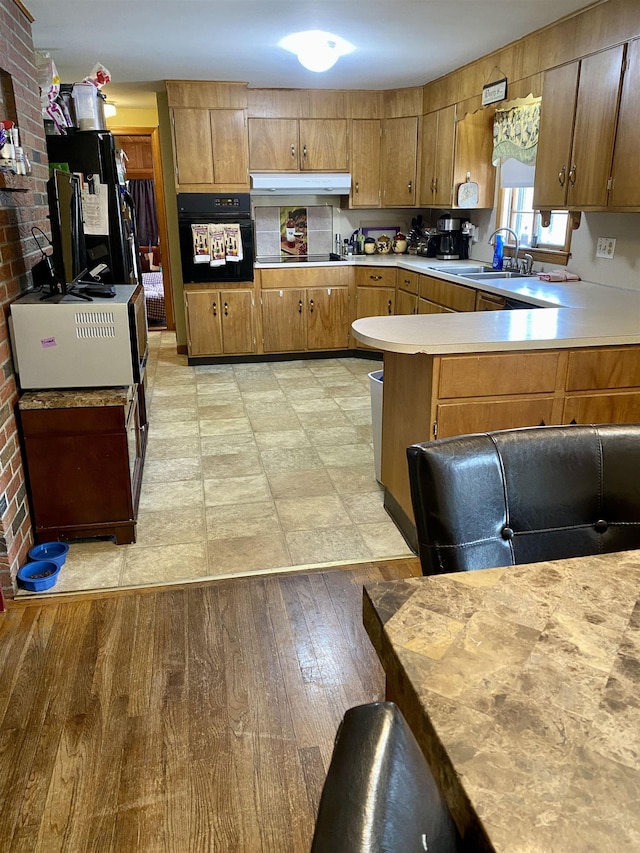 kitchen featuring black appliances, light countertops, light wood finished floors, and a sink