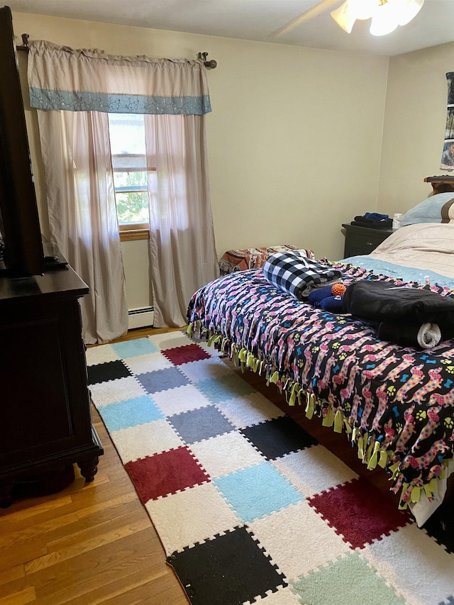 bedroom with a ceiling fan, a wood stove, wood finished floors, and baseboard heating