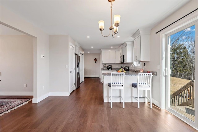 kitchen with a sink, dark wood-style floors, appliances with stainless steel finishes, and a peninsula