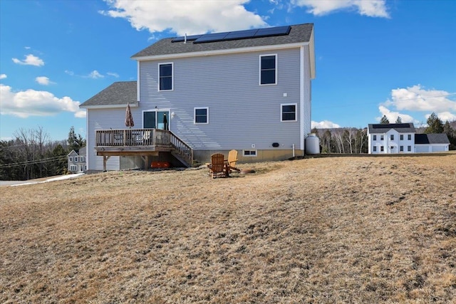 rear view of property featuring a wooden deck, roof mounted solar panels, and an outdoor fire pit