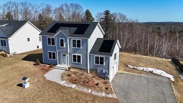 view of front of property featuring solar panels, a shingled roof, and a front lawn