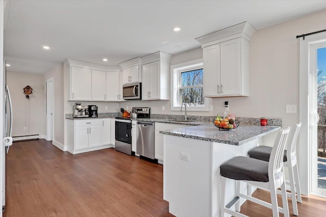 kitchen with a sink, stainless steel appliances, a peninsula, and white cabinets