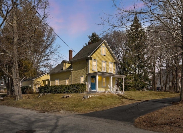 view of front of house with covered porch, a chimney, and a front lawn