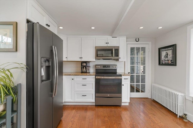 kitchen featuring light wood-type flooring, white cabinets, stainless steel appliances, and radiator heating unit