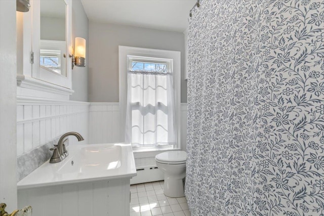 full bath with tile patterned flooring, toilet, baseboard heating, wainscoting, and a sink