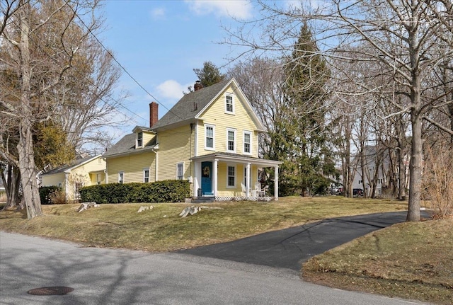 view of front of house with a front lawn, covered porch, and a chimney