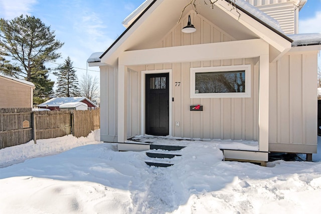 snow covered property entrance with fence and board and batten siding