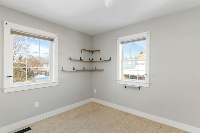 carpeted spare room featuring plenty of natural light, visible vents, and baseboards