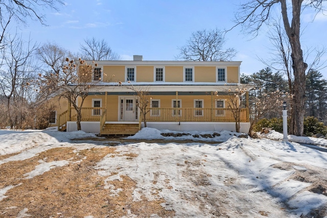 snow covered rear of property with covered porch and a chimney