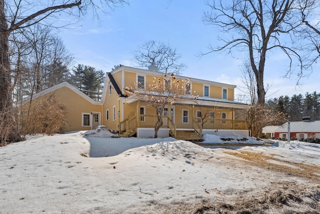 snow covered rear of property featuring a porch, a chimney, and a garage