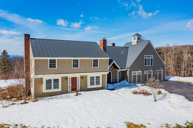 view of front of home with driveway, a standing seam roof, metal roof, a garage, and a chimney