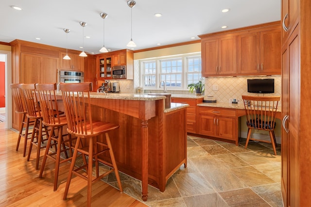 kitchen with brown cabinetry, appliances with stainless steel finishes, glass insert cabinets, and light stone counters