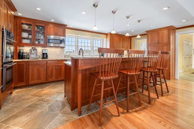 kitchen with light stone counters, brown cabinetry, ornamental molding, decorative backsplash, and appliances with stainless steel finishes