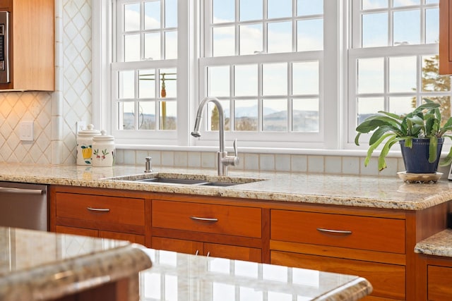 kitchen featuring dishwasher, light stone counters, brown cabinetry, plenty of natural light, and a sink