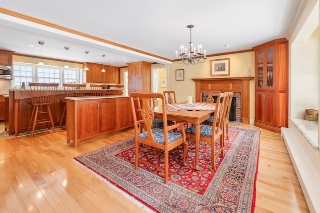 dining area featuring crown molding, a brick fireplace, a notable chandelier, and light wood-style floors