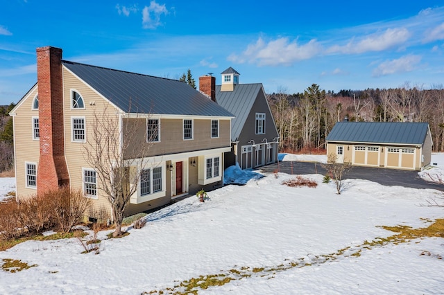 view of front of home featuring a detached garage, metal roof, an outbuilding, and a chimney