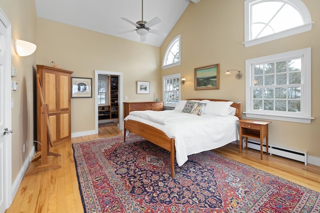 bedroom with a baseboard heating unit, baseboards, light wood-style floors, high vaulted ceiling, and a ceiling fan