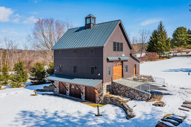 snow covered back of property featuring stone siding, an attached garage, and metal roof