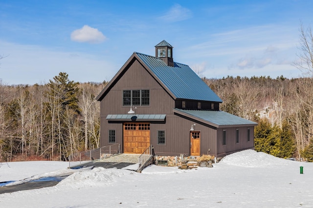 view of front of home featuring a standing seam roof, an outdoor structure, a garage, a view of trees, and metal roof