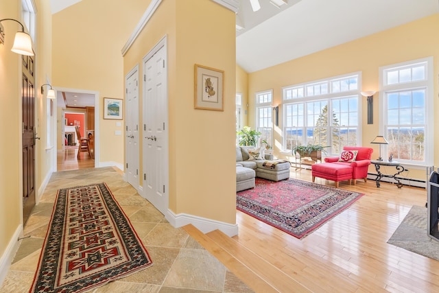 hall with a baseboard heating unit, light wood-style flooring, baseboards, and high vaulted ceiling