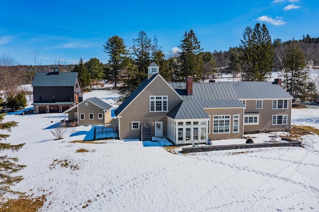 snow covered back of property featuring metal roof, central AC, a chimney, and a standing seam roof