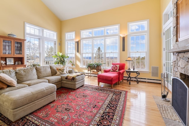 living room featuring high vaulted ceiling, light wood-style flooring, a fireplace, a baseboard radiator, and baseboard heating