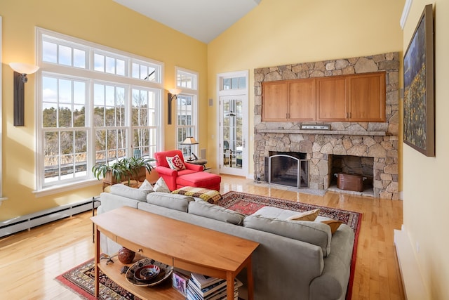 living area with light wood-type flooring, lofted ceiling, a stone fireplace, and a baseboard radiator