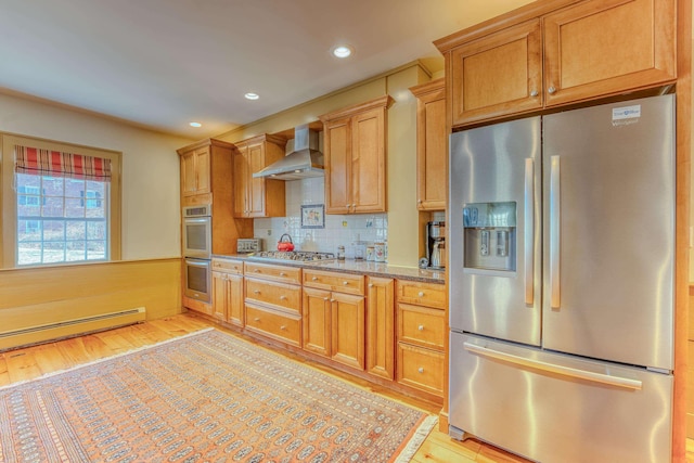 kitchen featuring wall chimney range hood, light stone countertops, wainscoting, light wood-style flooring, and stainless steel appliances