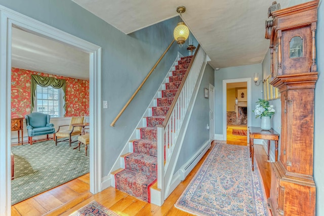 stairs featuring baseboard heating, wallpapered walls, baseboards, and wood-type flooring