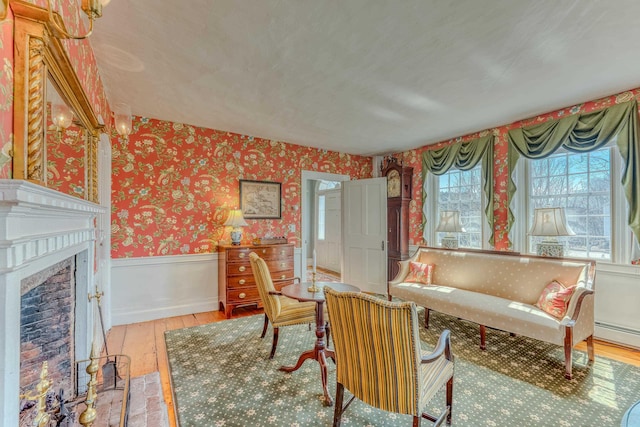 living room featuring wallpapered walls, hardwood / wood-style flooring, a fireplace with flush hearth, and a wainscoted wall