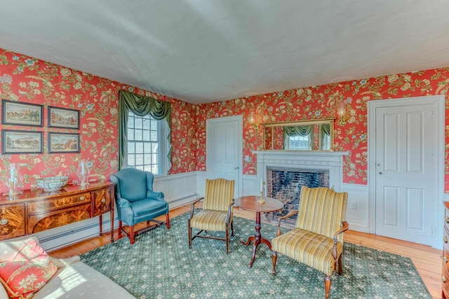 living area with wood finished floors, wallpapered walls, a fireplace, wainscoting, and baseboard heating