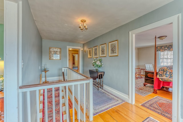 hallway with an upstairs landing, baseboards, and wood finished floors