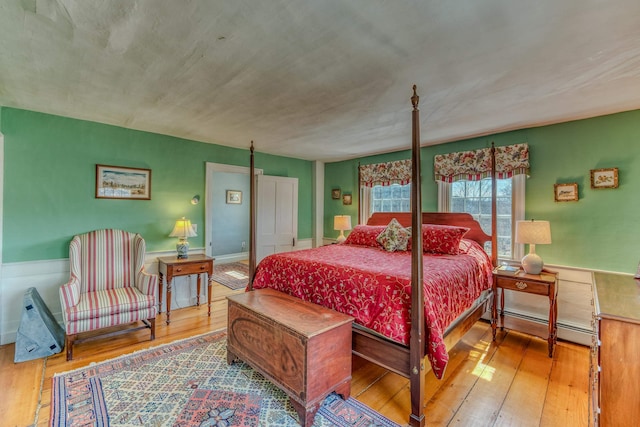 bedroom featuring a baseboard heating unit, a wainscoted wall, and wood-type flooring