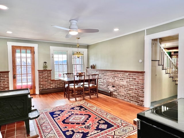 dining area with brick wall, wood finished floors, ceiling fan, and ornamental molding