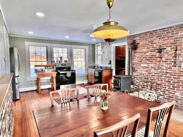 dining room featuring light wood finished floors, a wood stove, a baseboard heating unit, crown molding, and baseboard heating