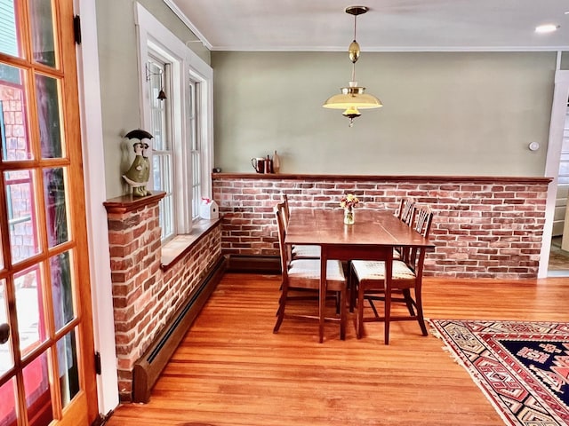 dining area featuring ornamental molding, light wood-style floors, brick wall, baseboard heating, and a healthy amount of sunlight