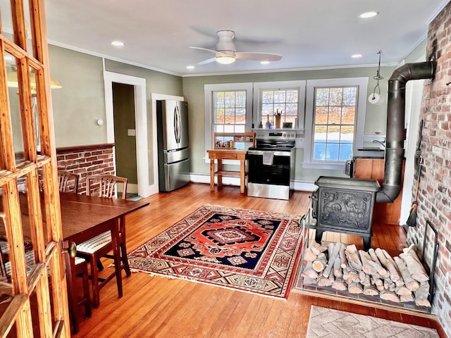 living area with a baseboard heating unit, wood finished floors, a wood stove, and crown molding