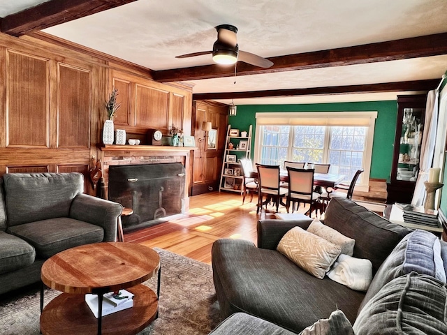 living room featuring beamed ceiling, a ceiling fan, a fireplace, and light wood finished floors