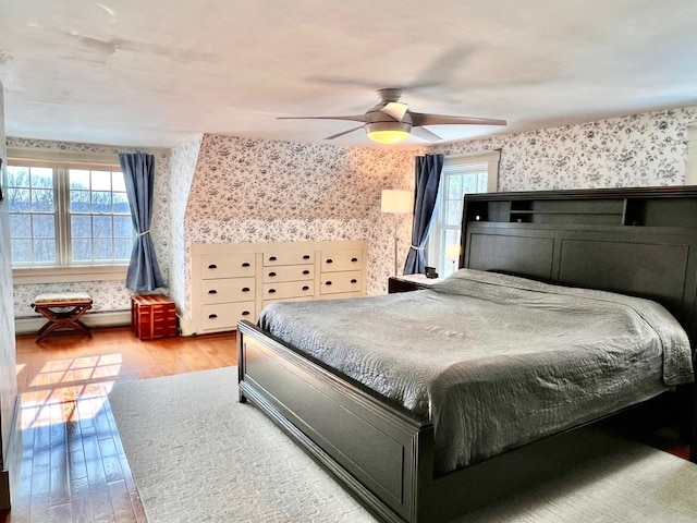 bedroom featuring wallpapered walls, multiple windows, wood finished floors, and a ceiling fan