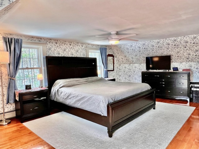 bedroom with wallpapered walls, wood finished floors, baseboard heating, and a ceiling fan