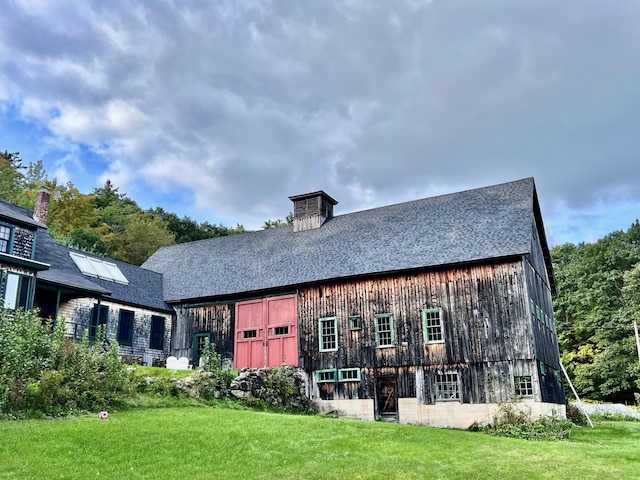 rear view of house with a barn, a yard, an outbuilding, and roof with shingles