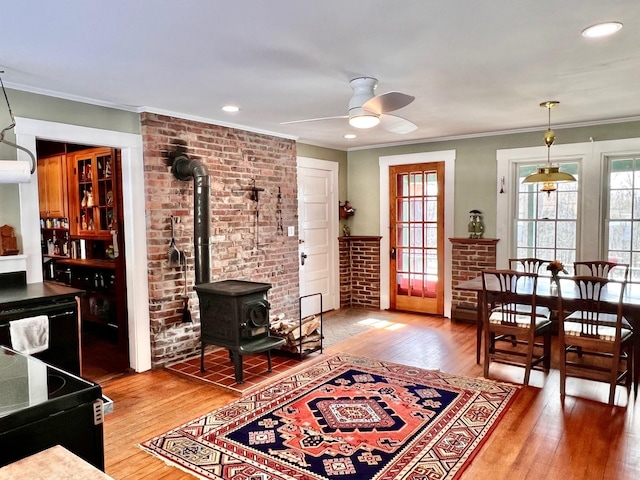 living area featuring brick wall, ornamental molding, a wood stove, light wood-style floors, and a ceiling fan